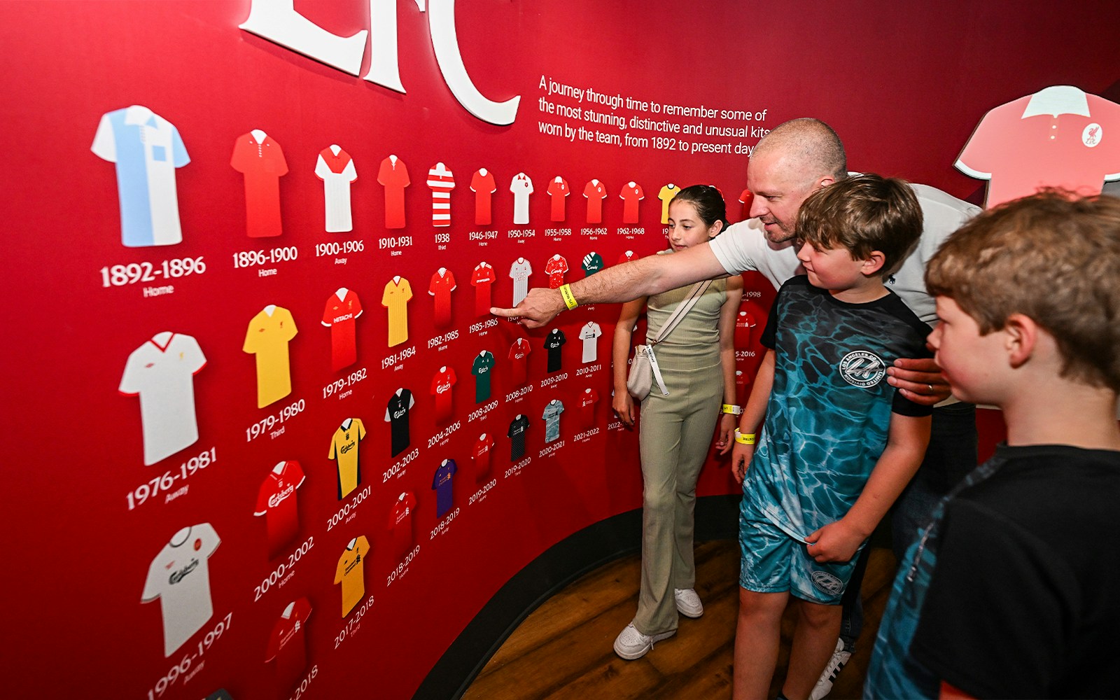 Visitors explore Liverpool FC jersey history display at Anfield Stadium.