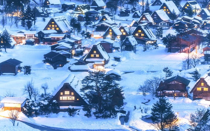 Traditional gassho-zukuri houses in snow-covered Shirakawa-go village, illuminated at dusk.