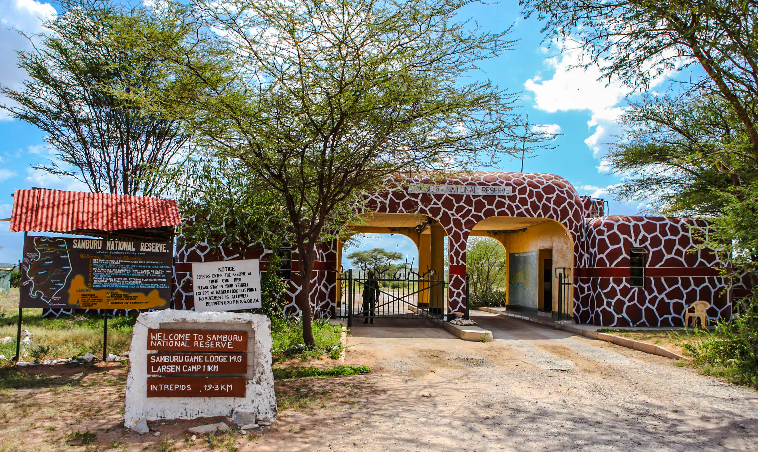 Entrance to Samburu National Reserve, featuring giraffe-patterned gate and informational signs, Kenya.