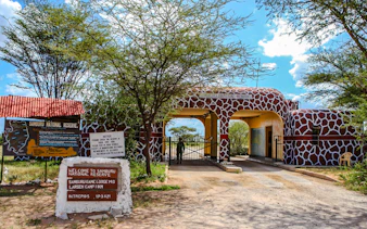 Entrance to Samburu National Reserve, featuring giraffe-patterned gate and informational signs, Kenya.