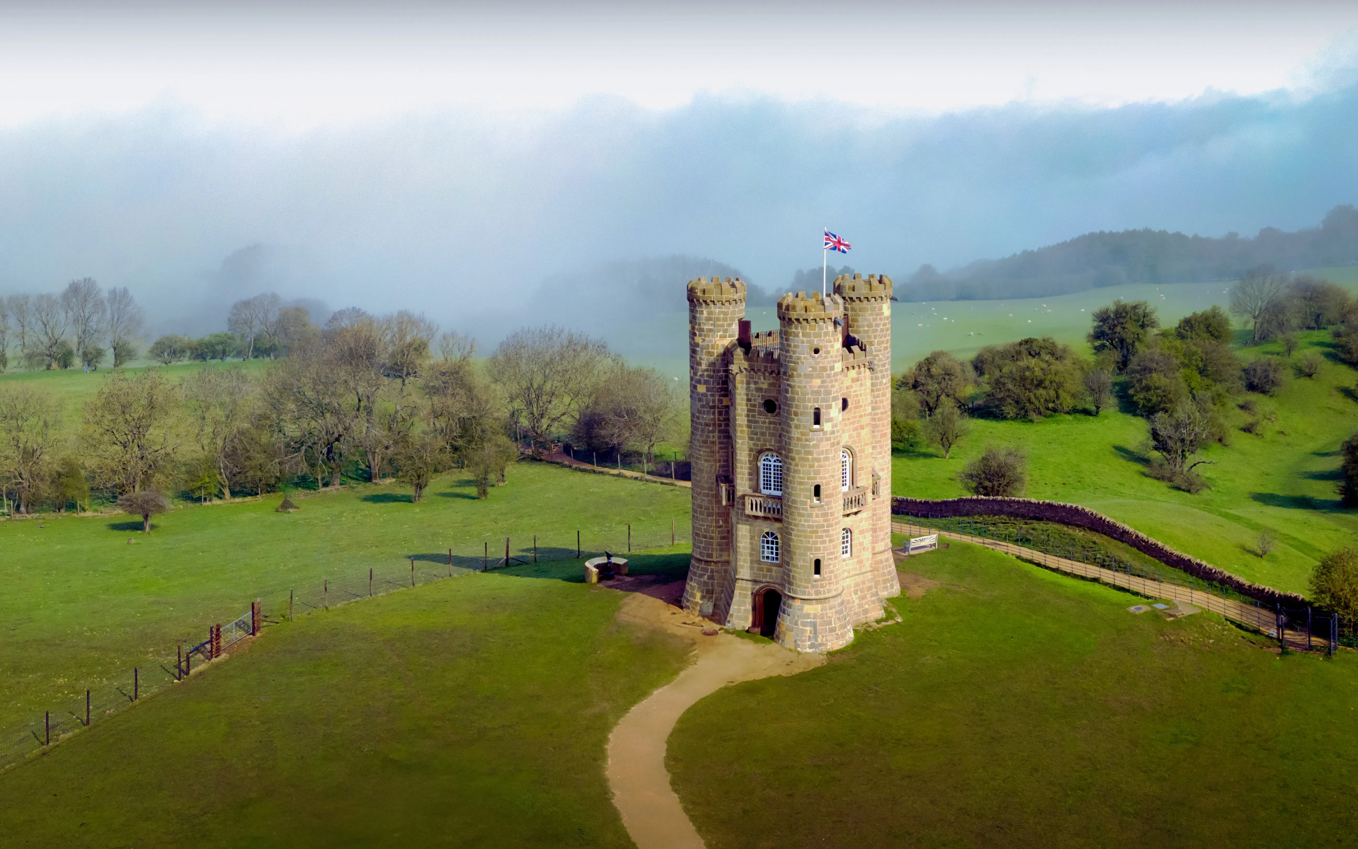 Broadway Tower in Cotswolds, UK, surrounded by green fields and misty landscape.