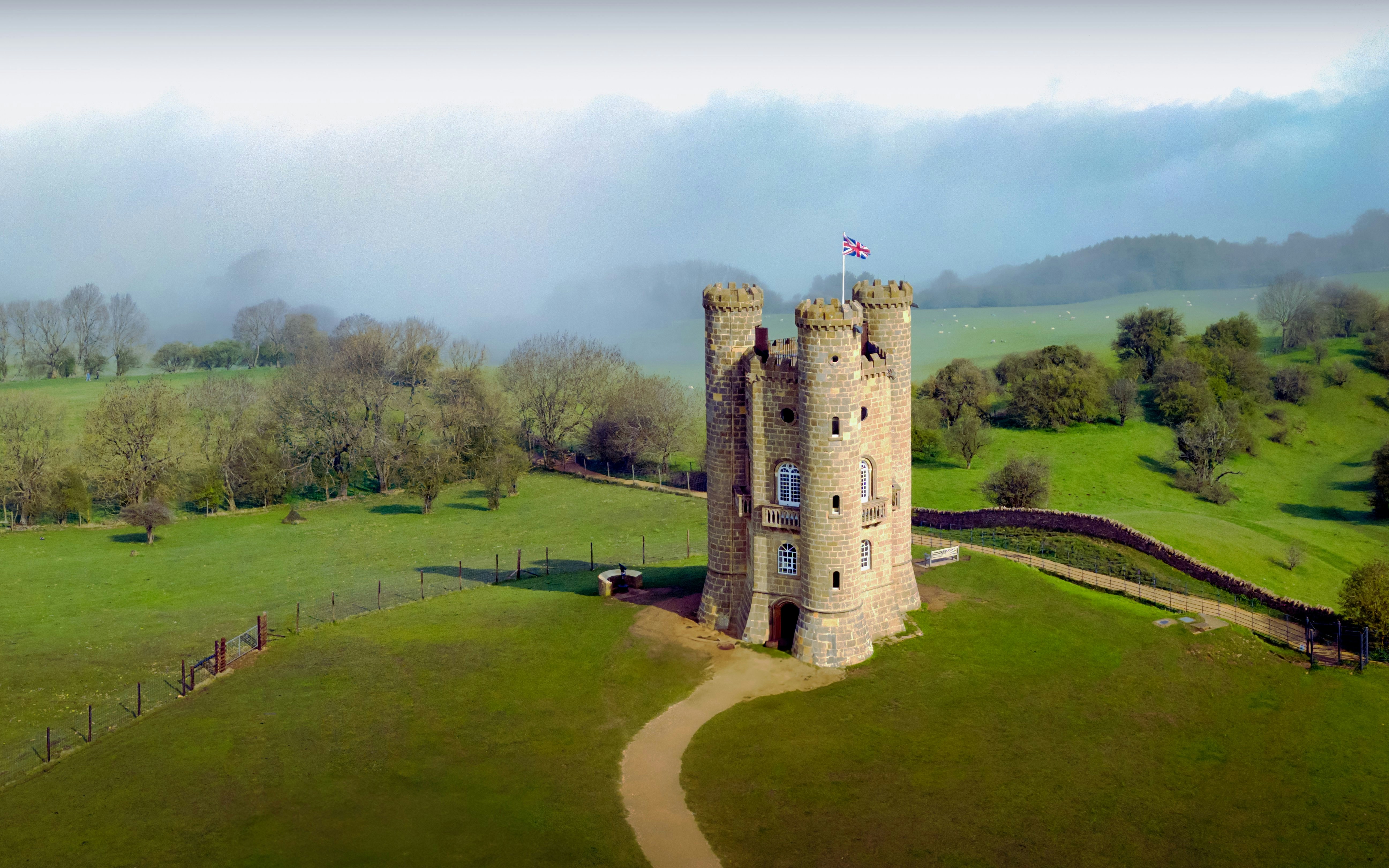 Broadway Tower in Cotswolds, UK, surrounded by green fields and misty landscape.
