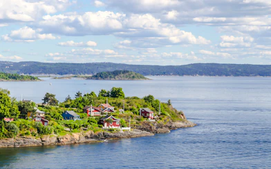 Cottages on a lush island in the Oslo fjord, Norway, surrounded by water and distant hills.