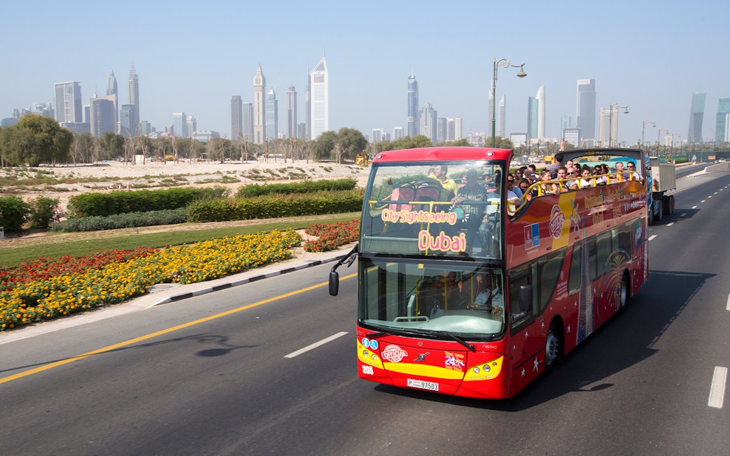 Open-top sightseeing bus in Dubai with city skyline in the background.