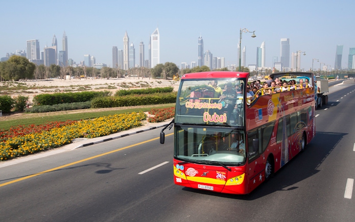 Open-top sightseeing bus in Dubai with city skyline in the background.
