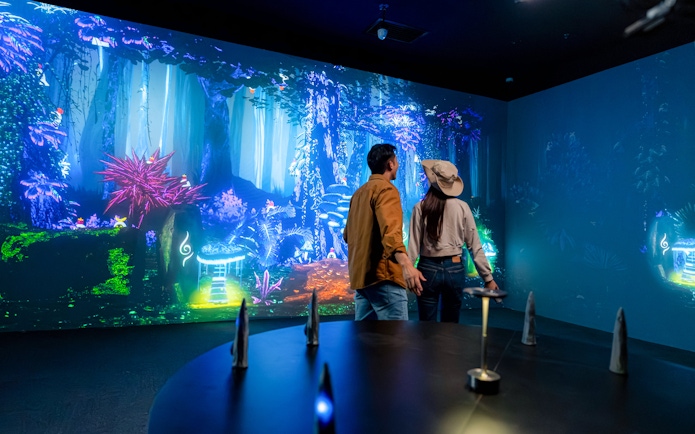 Tourists viewing colorful digital forest display at Enchanted Forest exhibit.