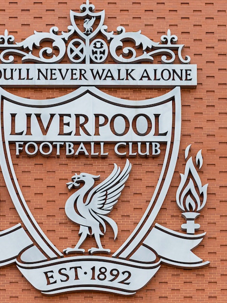 Abseiler descending Anfield Stadium wall beside Liverpool FC crest.