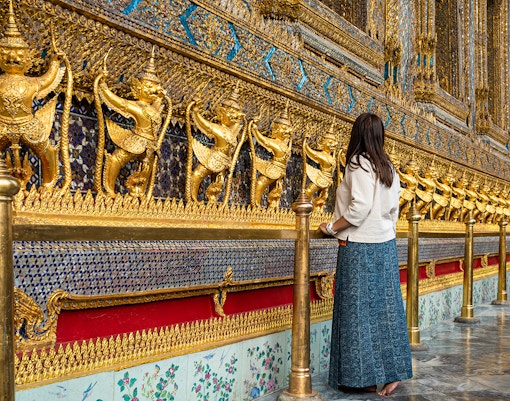 Woman admiring ornate golden garuda statues at Bangkok's Grand Palace.