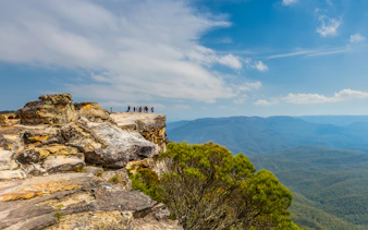 Group of people standing on Lincoln’s Rock, Blue Mountains, overlooking vast forested landscape.