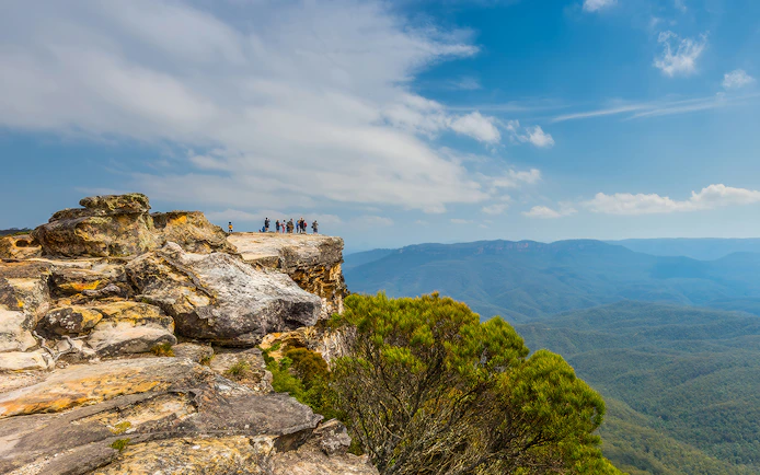 Group of people standing on Lincoln’s Rock, Blue Mountains, overlooking vast forested landscape.