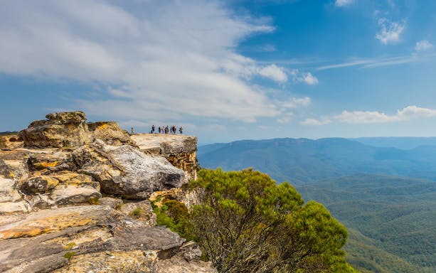 Group of people standing on Lincoln’s Rock, Blue Mountains, overlooking vast forested landscape.