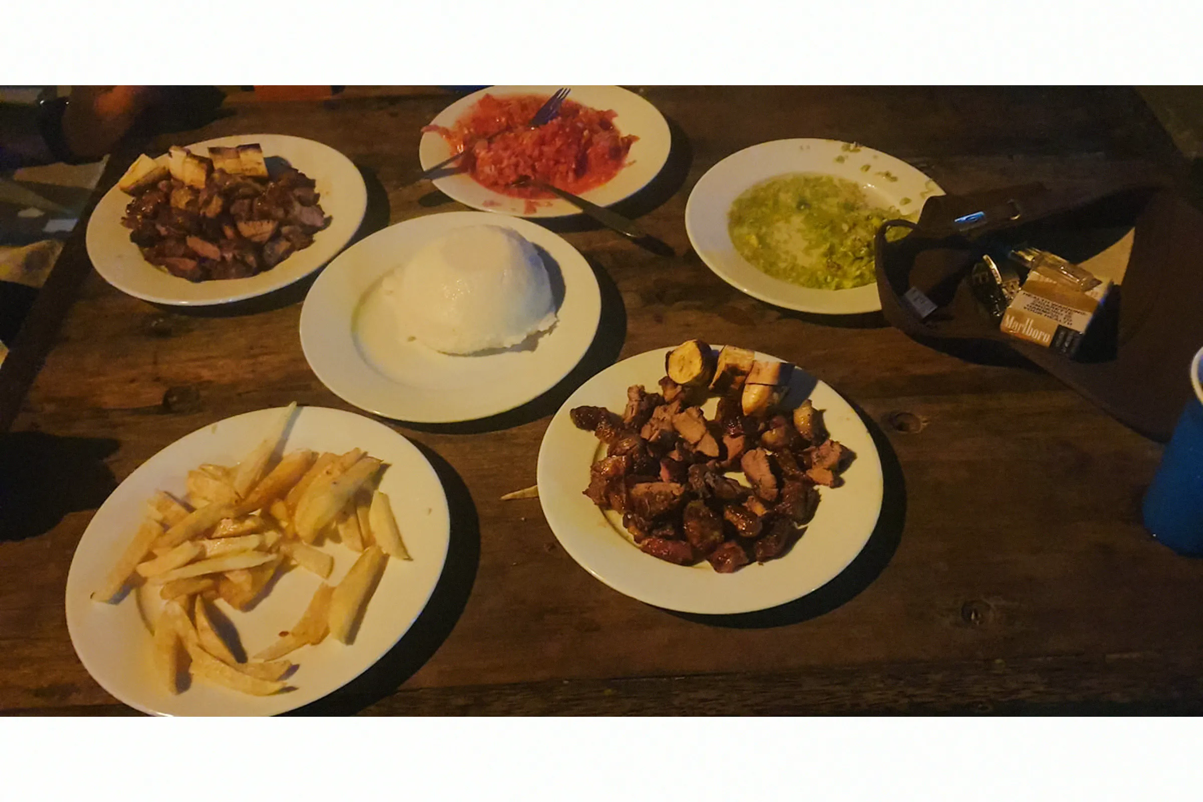Traditional Zanzibar meal with grilled meat, fries, and local sauces on a wooden table.
