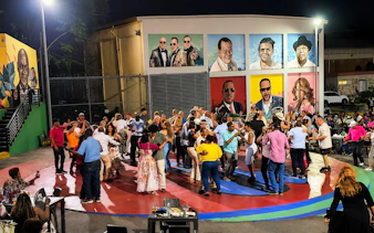 People dancing to live Caribbean music in Santo Domingo, with vibrant murals in the background.