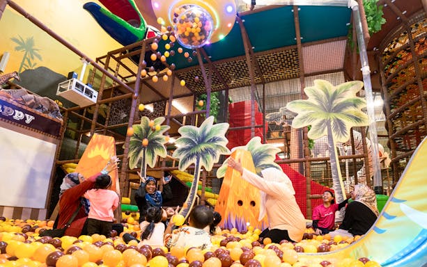 Children playing in a colorful ball pit at Safari Escape Playland with palm tree decorations.