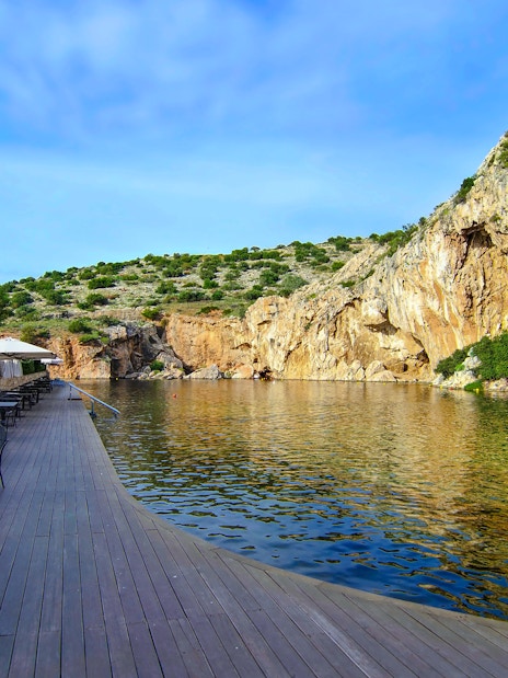 Vouliagmeni Lake in Attica, Greece with waterside dining area and rocky cliffs.