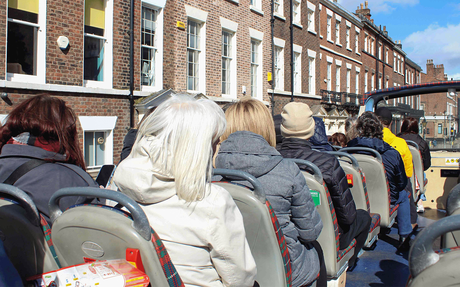 Passengers on open-top bus tour in Liverpool city.