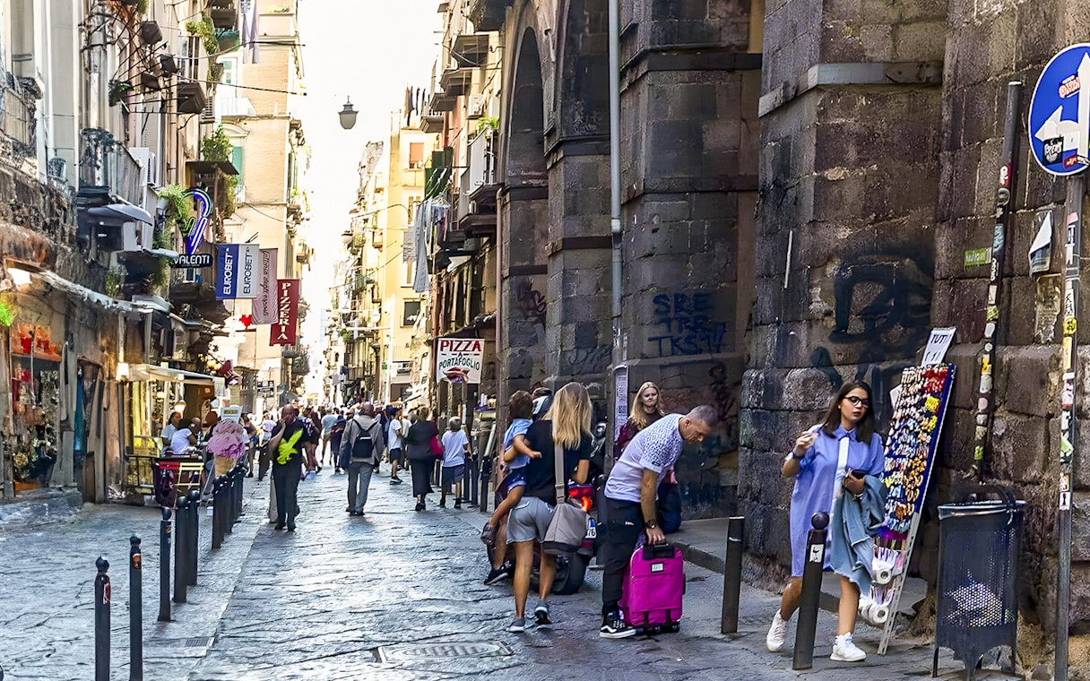 Exploring bustling historic alley in Naples with shops and tourists.
