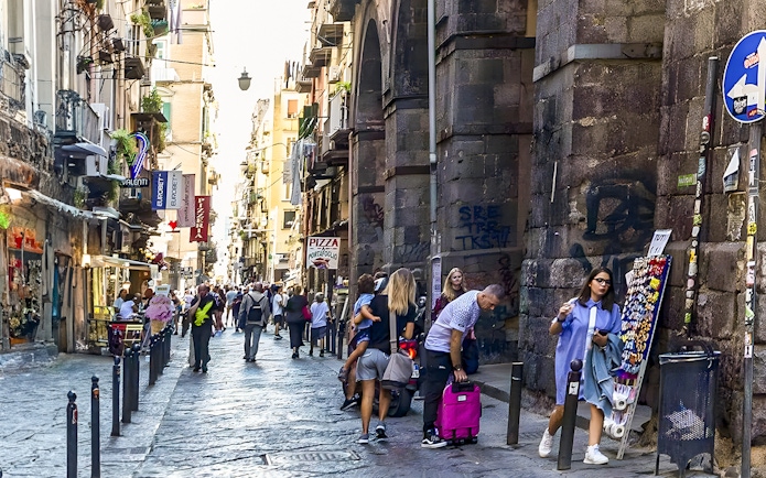Exploring bustling historic alley in Naples with shops and tourists.