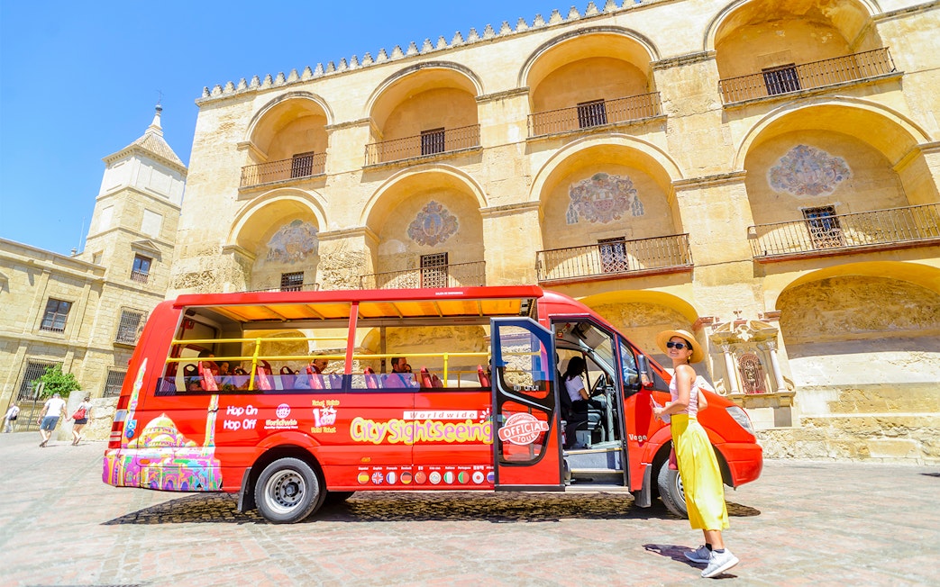 Woman waiting outside hop-on hop-off mini bus in front of historic building in Córdoba, Spain.