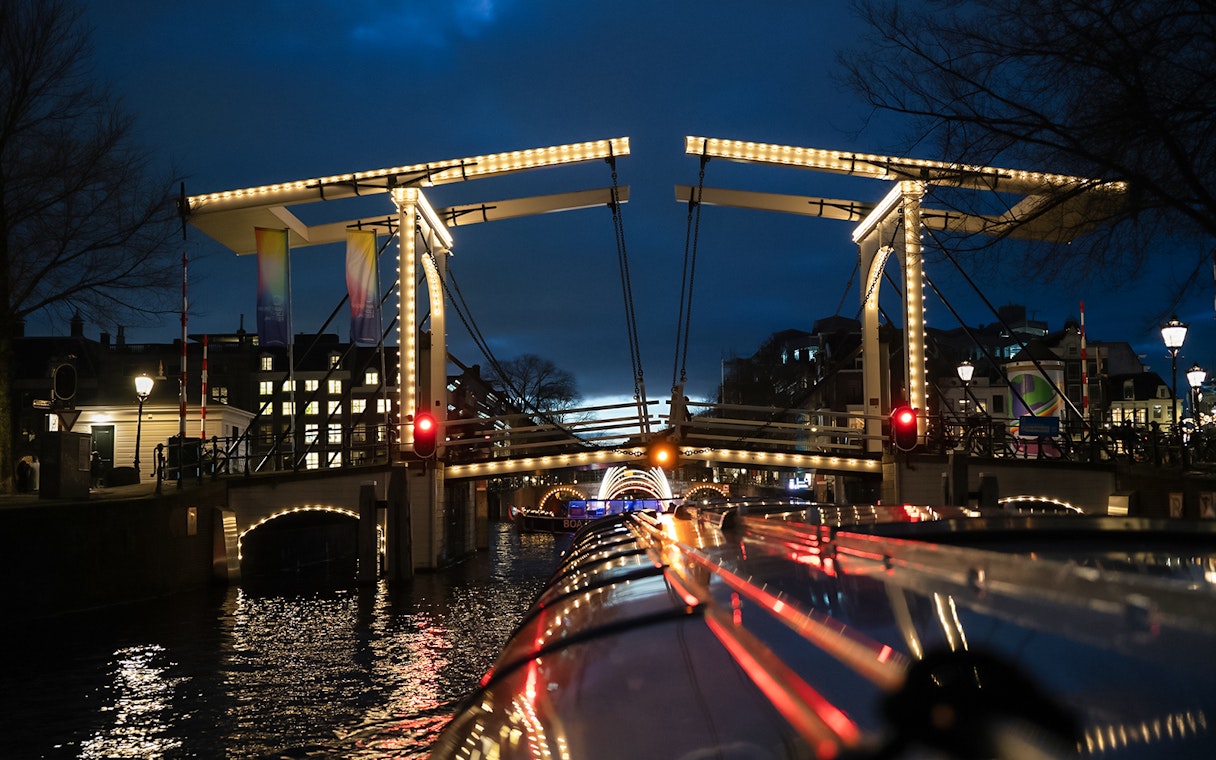 Illuminated bridge over canal during Amsterdam Light Festival cruise.