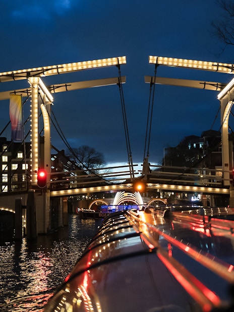 Illuminated bridge over canal during Amsterdam Light Festival cruise.