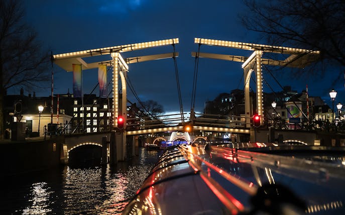 Illuminated bridge over canal during Amsterdam Light Festival cruise.