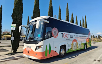 Tootbus Tuscany tour bus parked near cypress trees in Tuscany, Italy.