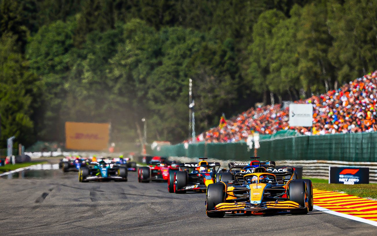 Formula 1 cars racing at the Belgian Grand Prix 2023 with spectators in the background.