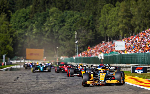 Formula 1 cars racing at the Belgian Grand Prix 2023 with spectators in the background.