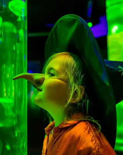 Child in costume observing jellyfish at Sea Life Scheveningen aquarium.