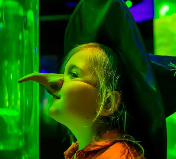 Child in costume observing jellyfish at Sea Life Scheveningen aquarium.