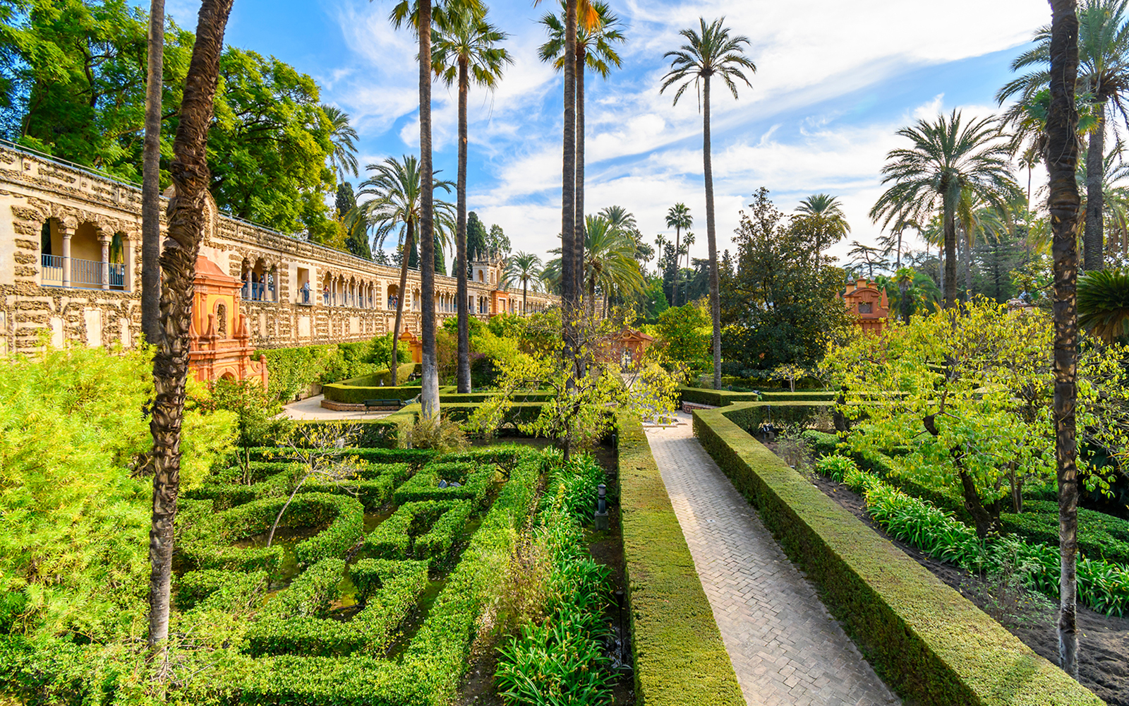 Seville Alcazar Gardens with intricate hedges and vibrant flowers in a historic courtyard setting.