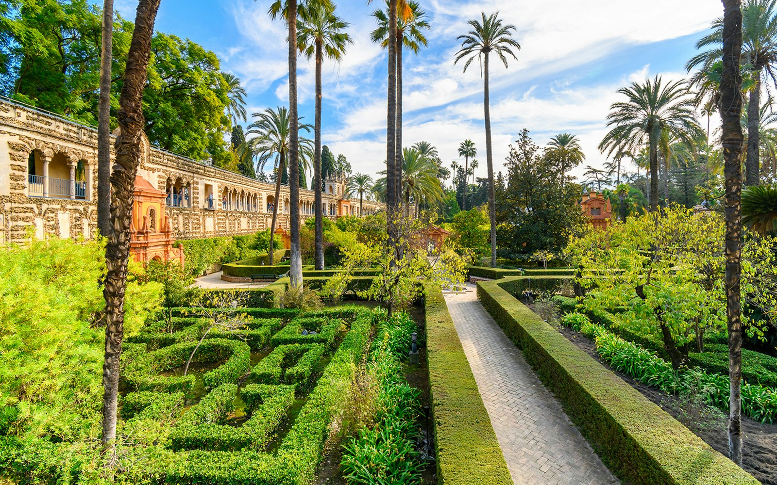 Seville Alcazar Gardens with intricate hedges and vibrant flowers in a historic courtyard setting.