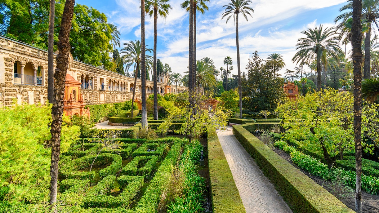 Seville Alcazar Gardens with intricate hedges and vibrant flowers in a historic courtyard setting.