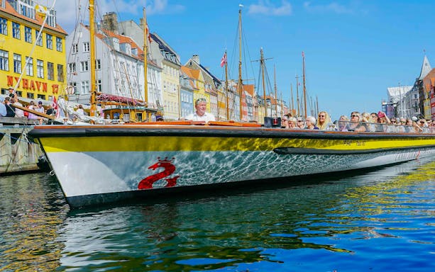Canal cruise boat with tourists in Nyhavn, Copenhagen, colorful buildings in the background.