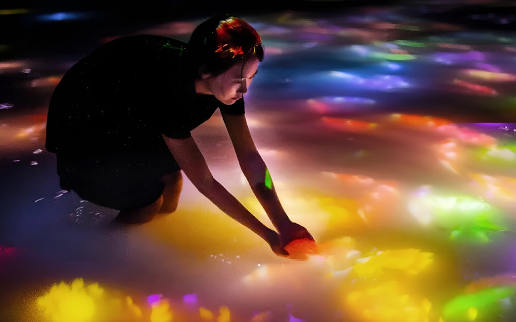 Person interacting with colorful digital koi and flowers at teamLab Tokyo.