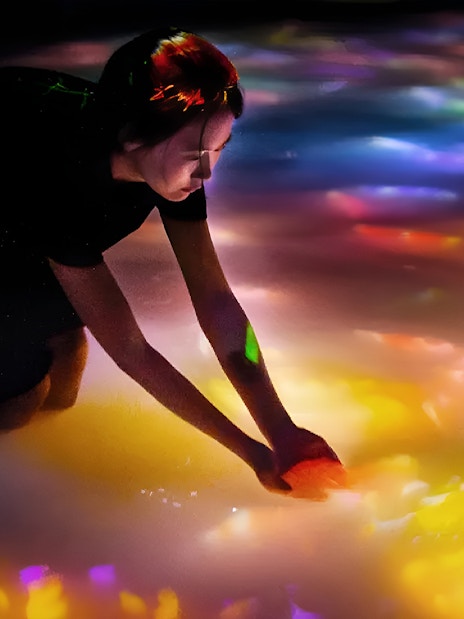 Person interacting with colorful digital koi and flowers at teamLab Tokyo.