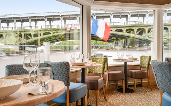 Seine River dinner cruise interior with view of Paris bridge and French flag.