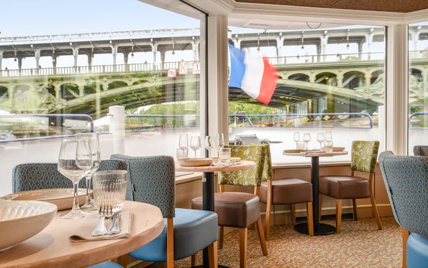 Seine River dinner cruise interior with view of Paris bridge and French flag.