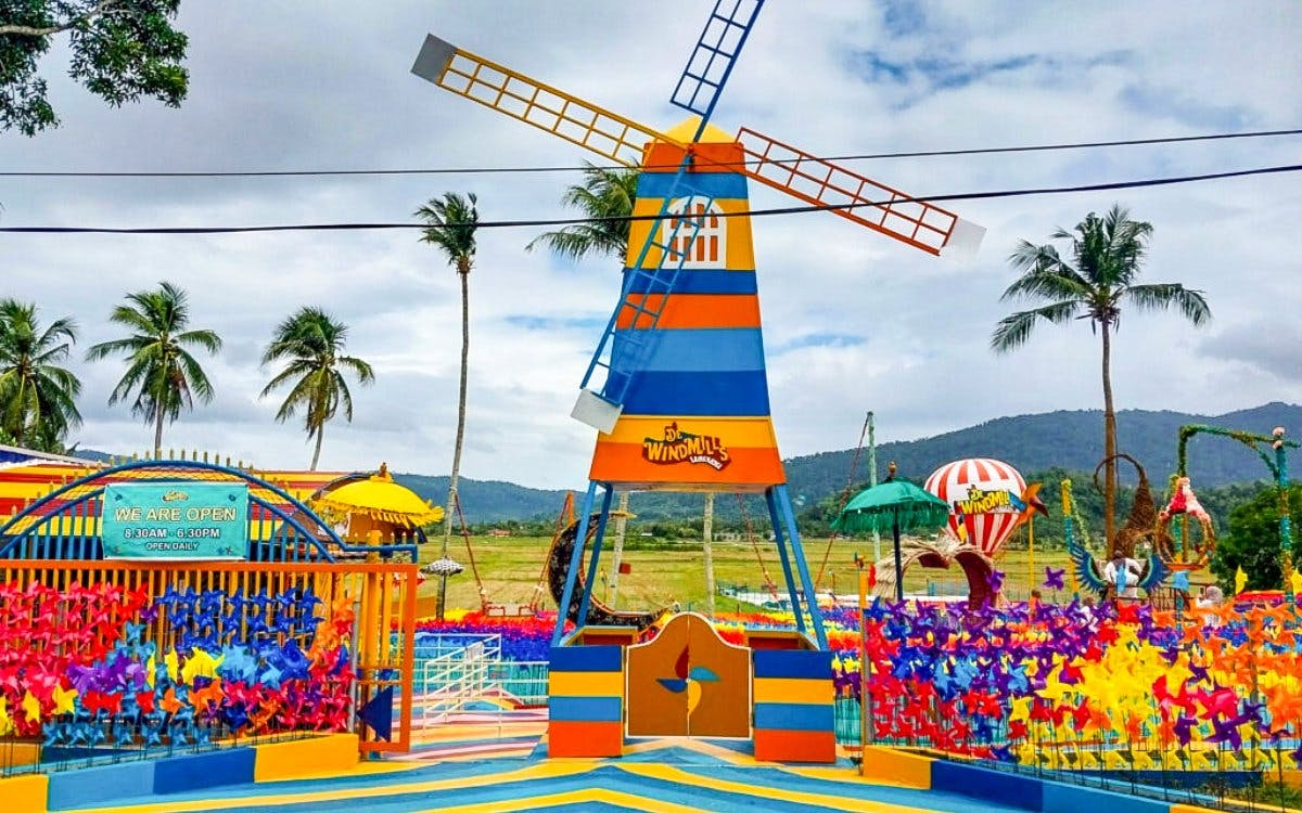 Colorful windmill structure at De Windmill Selfie Park with palm trees and mountains in the background.