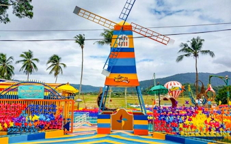 Colorful windmill structure at De Windmill Selfie Park with palm trees and mountains in the background.