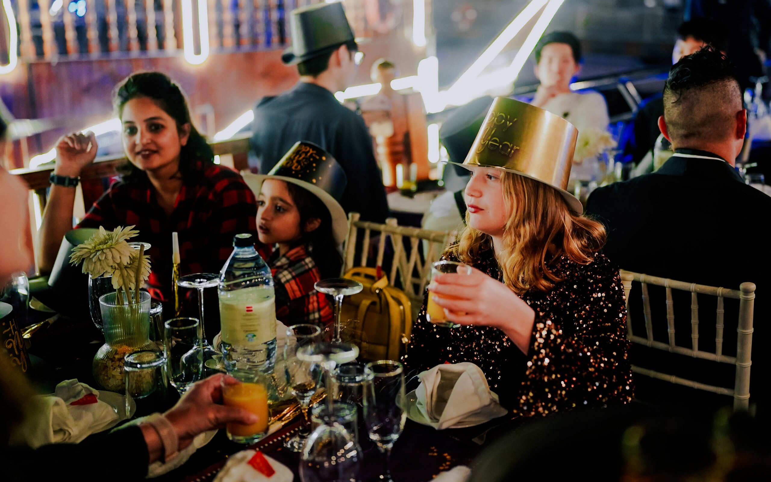 Guests celebrating on a New Year's Eve Creek Dhow Dinner Cruise, wearing festive hats and enjoying drinks.