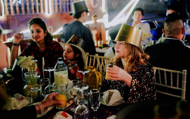 Guests celebrating on a New Year's Eve Creek Dhow Dinner Cruise, wearing festive hats and enjoying drinks.