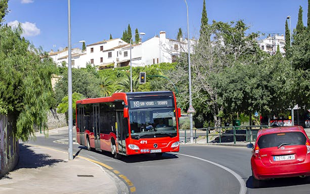 Red bus on route N9 in Granada, Spain, near residential area with greenery.