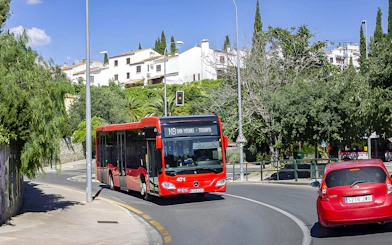 Granada city bus on route near Alsa station, surrounded by greenery and buildings.