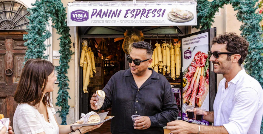 Guide serving panini to guests at a Rome food tour outside a deli.