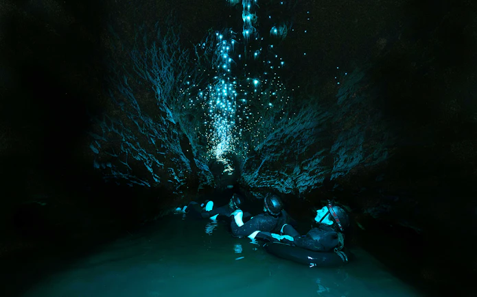 Visitors floating in Okohua Glowworm Cave, illuminated by glowworms, Waitomo Experience.