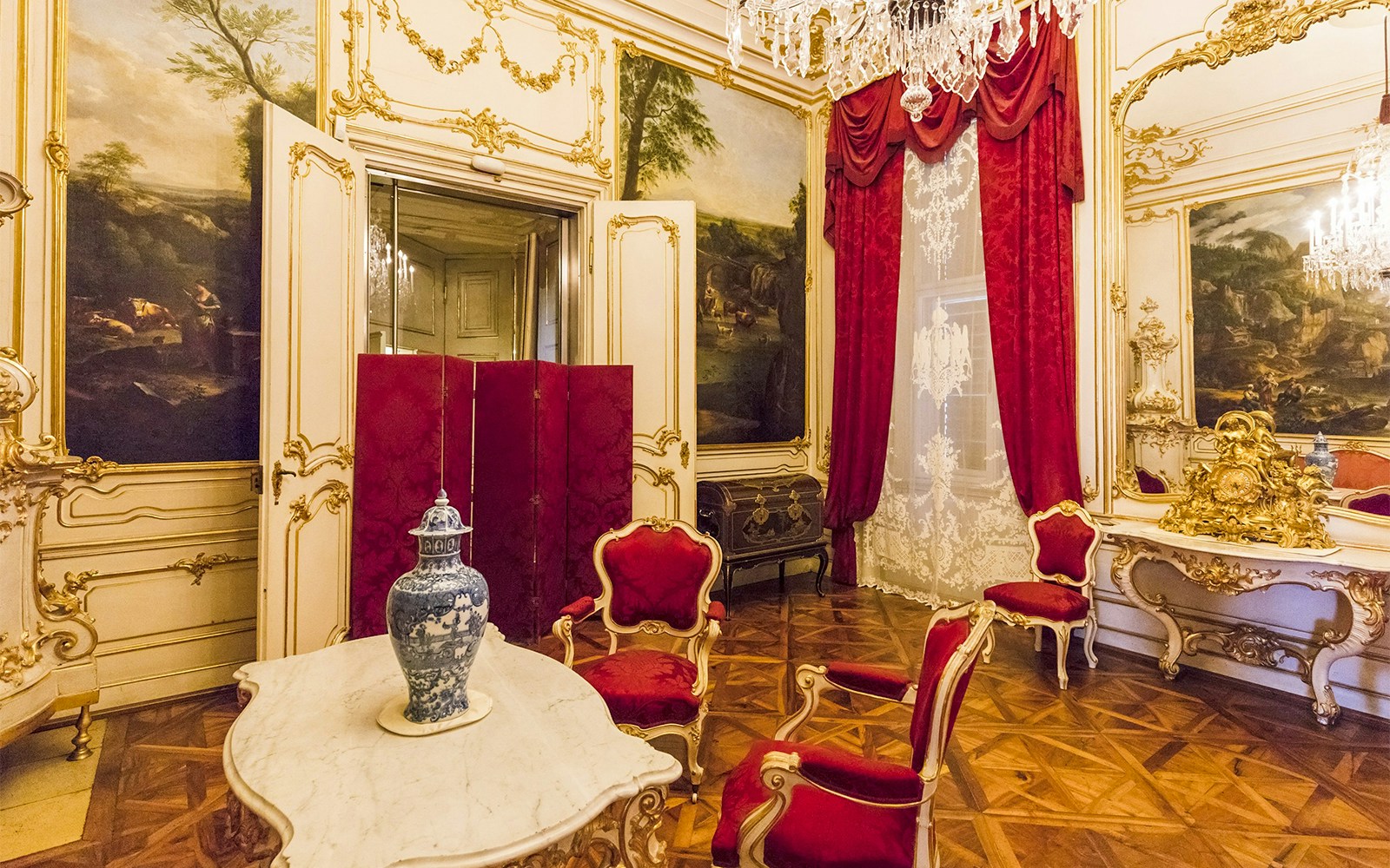 Elegant room in Schönbrunn Palace, Vienna, featuring ornate decor and red velvet chairs.