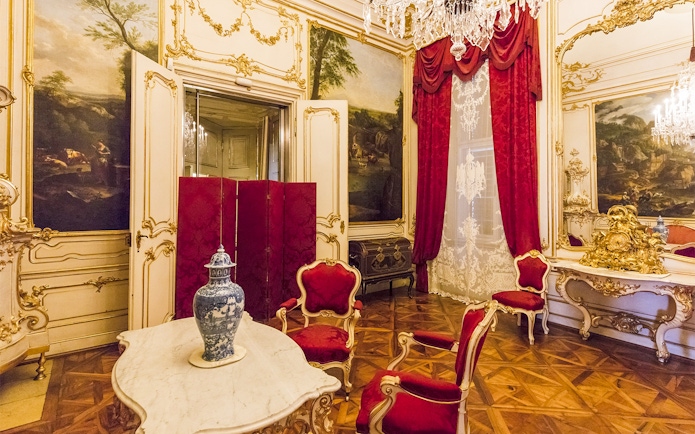 Elegant room in Schönbrunn Palace, Vienna, featuring ornate decor and red velvet chairs.