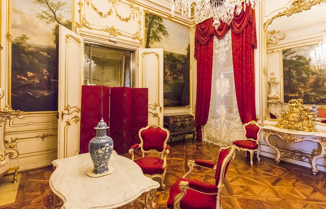 Elegant room in Schönbrunn Palace, Vienna, featuring ornate decor and red velvet chairs.